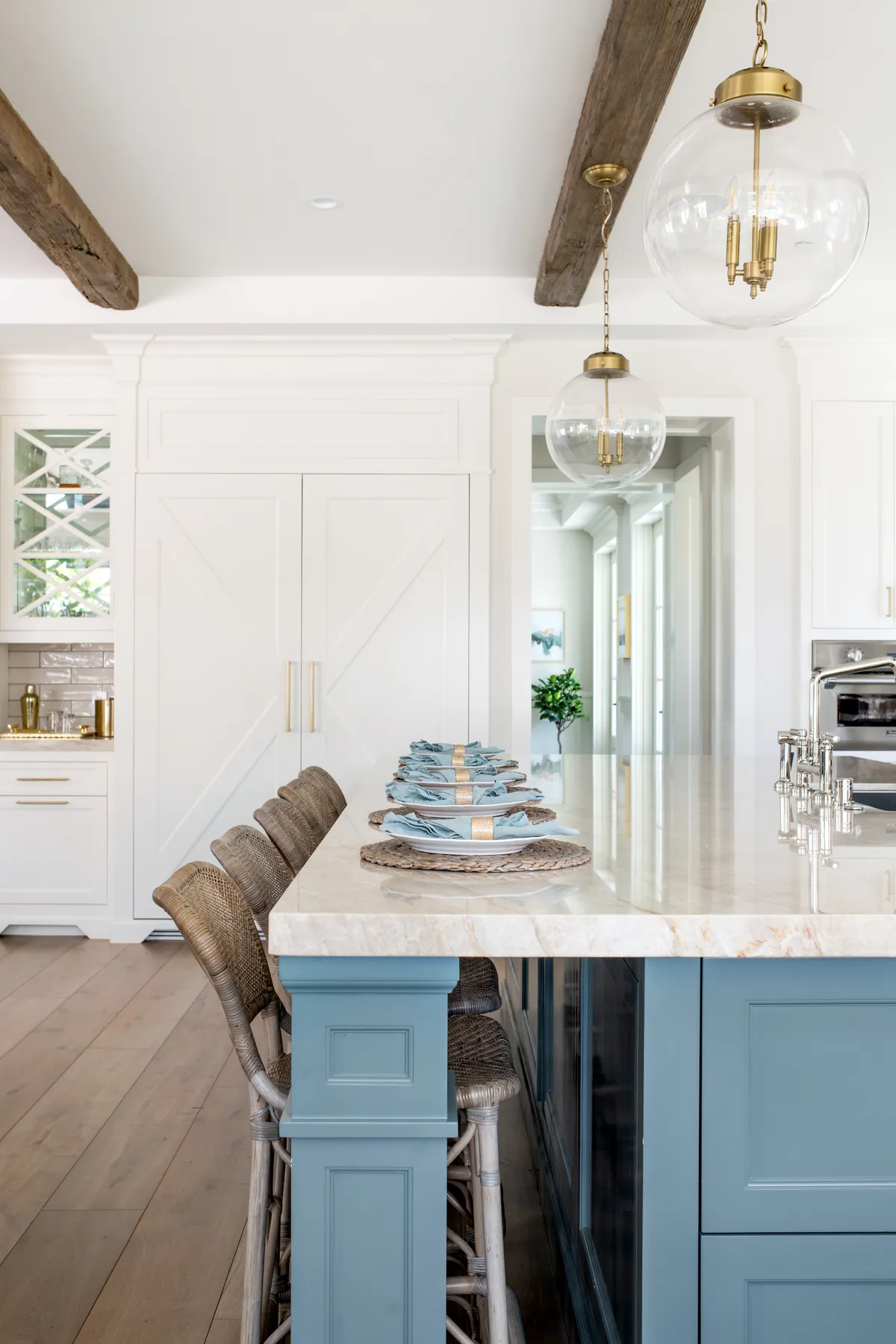 Brass hardware and woven counter stools around a deep-blue island in a white coastal kitchen, our coastal-contemporary eye at work.