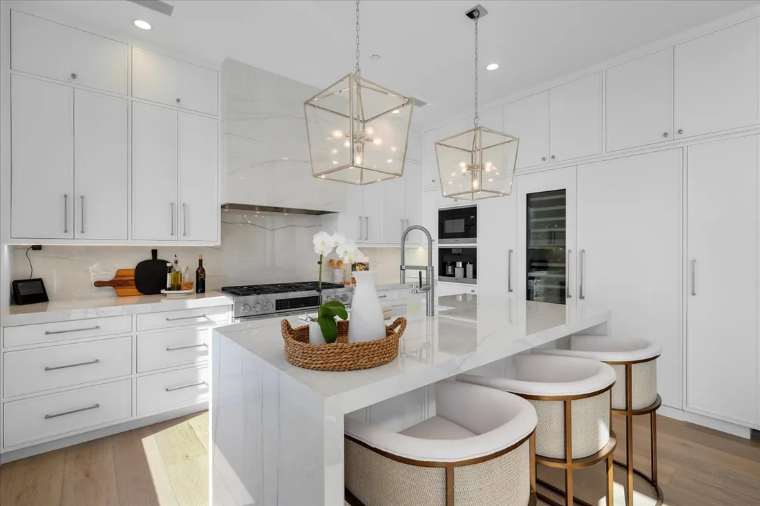 Panel-ready refrigeration and a waterfall quartzite island under lantern pendants in a bright white marble kitchen.
