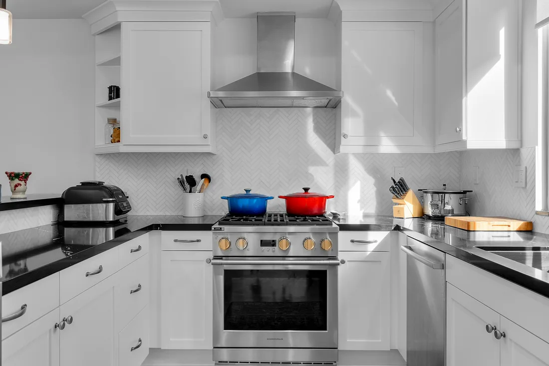 A white marble herringbone backsplash sets off a Wolf gas range in a freshly remodeled white kitchen.