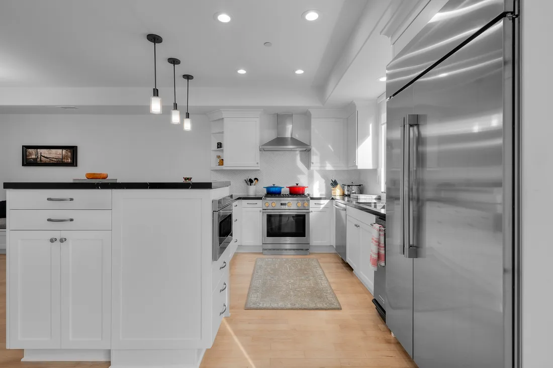 A Sub-Zero refrigerator and Wolf range anchor a white shaker kitchen lit by industrial pendant lighting.