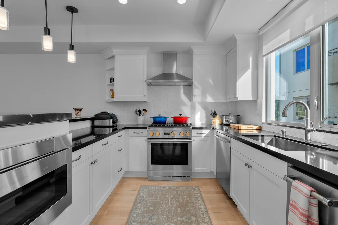 Black countertops and a marble herringbone backsplash frame a stainless Wolf range in a crisp white kitchen.