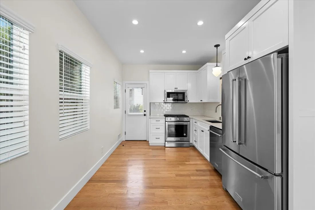 White shaker cabinetry runs both walls of a compact galley kitchen with stainless appliances and light hardwood floors.